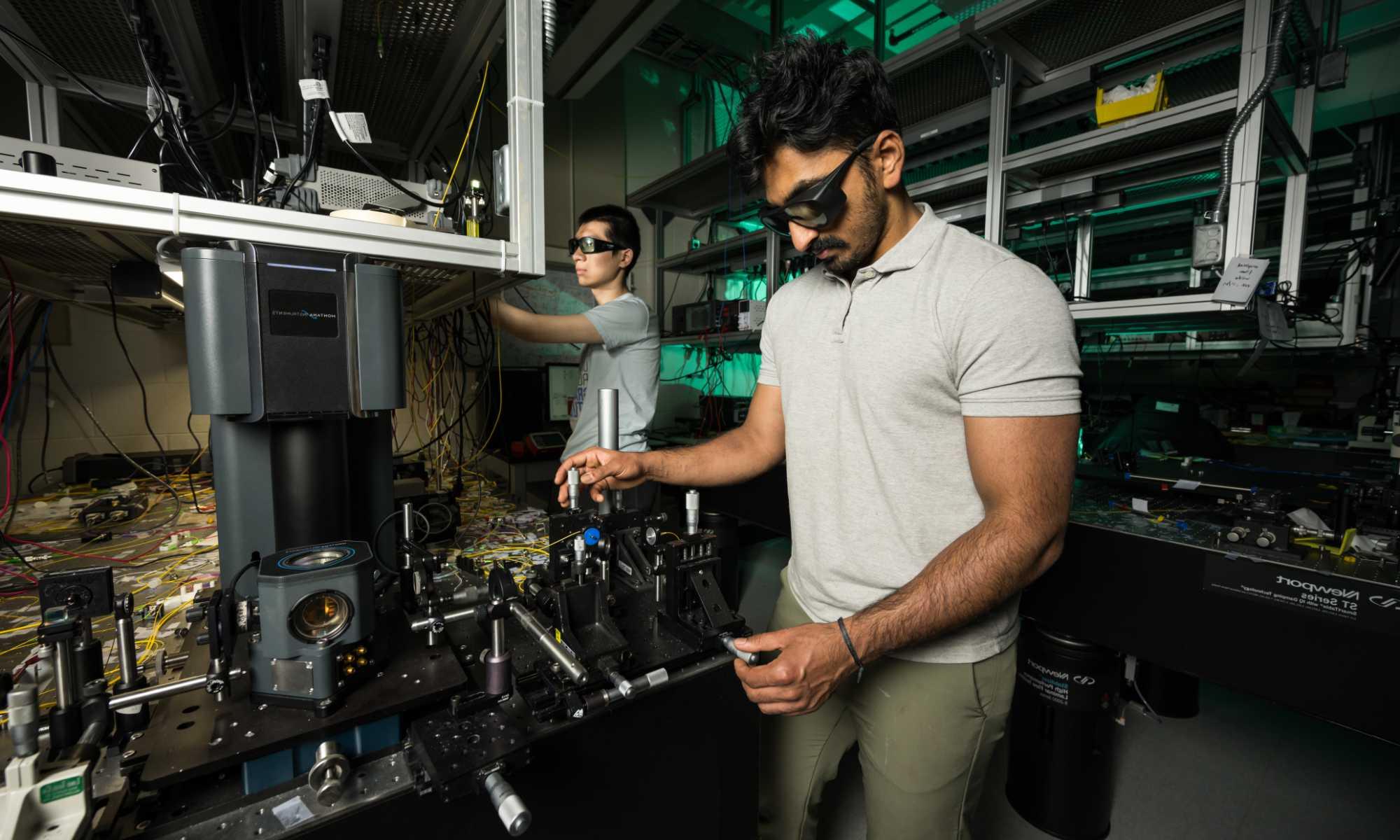 Two researchers wearing protective eyewear manipulate the equipment in an optics lab to produce surface acoustic waves.