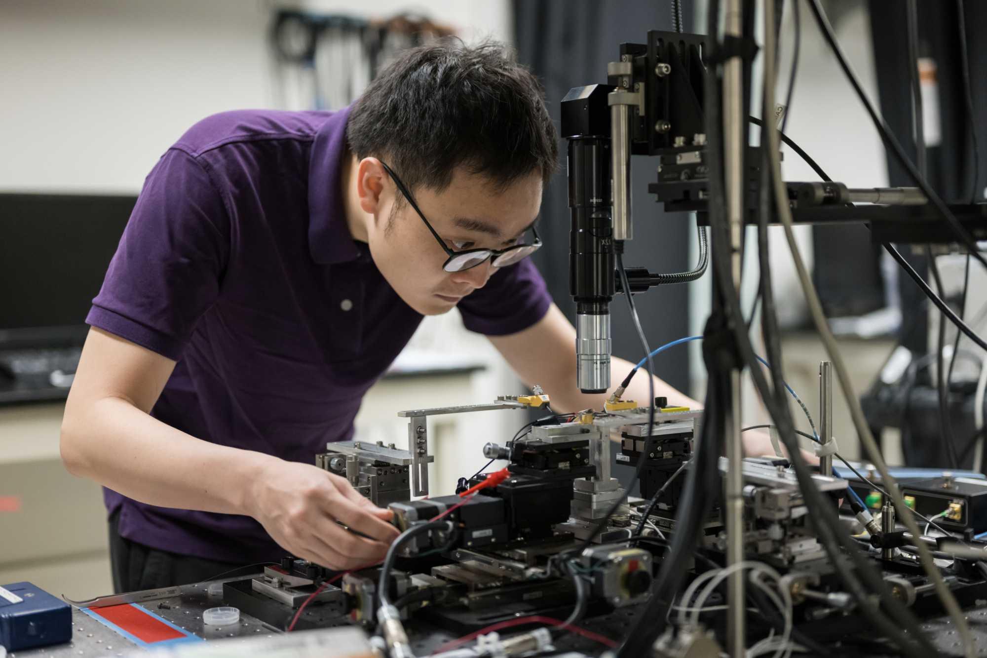 A graduate student adjust a new "all in one" microcomb laser device in a lab.